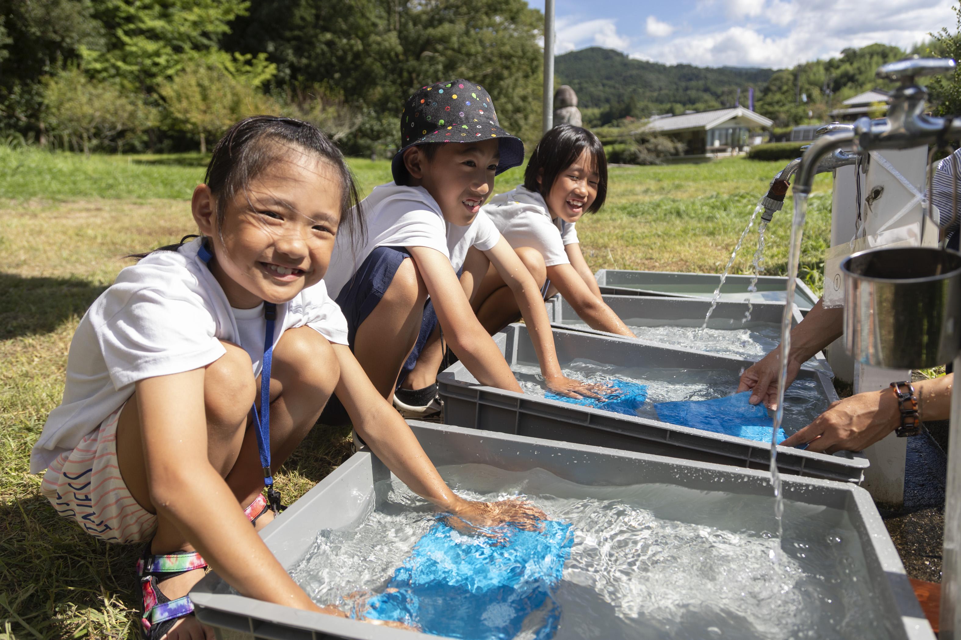 資料館の庭で流水で印画紙を洗う子供3人の画像