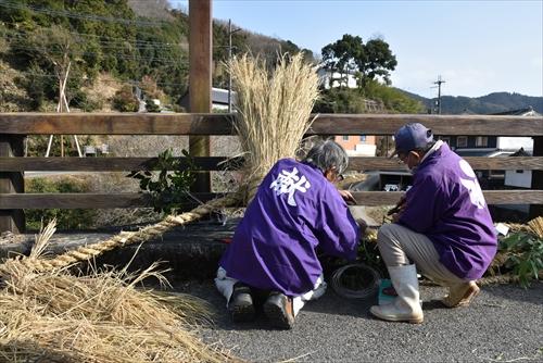 献と書かれた紫の法被を着た男性二人がおづなに榊と御幣を取り付けている写真