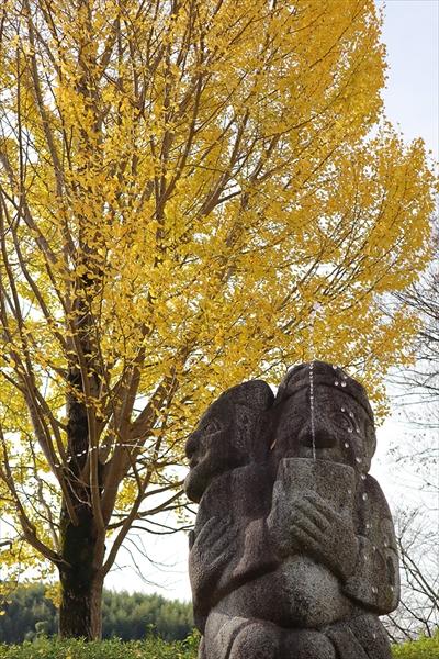 庭の石人像と黄色いイチョウの木の画像